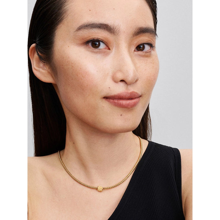 A woman wearing a gold-plated necklace with a textured four-leaf clover charm at the center.