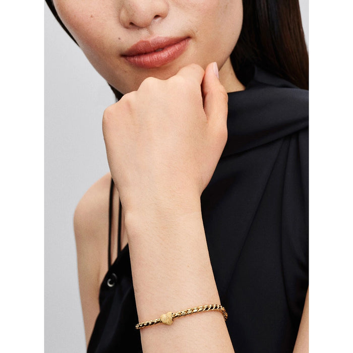 A woman wearing a gold chain bracelet adorned with the textured gold heart-shaped charm, styled with a sleeveless black top.