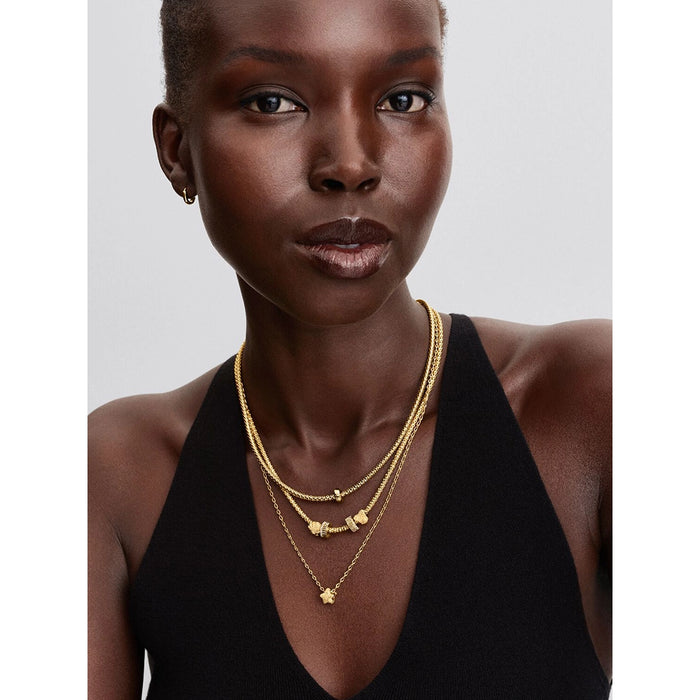 Model wearing layered gold necklaces featuring Pandora Textured Star Charm pendant styled with other gold charms.