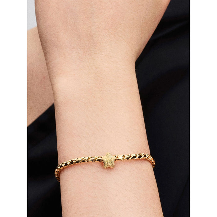 Pandora Shimmering Star Charm in gold styled on a chunky gold chain bracelet, shown on wrist.
