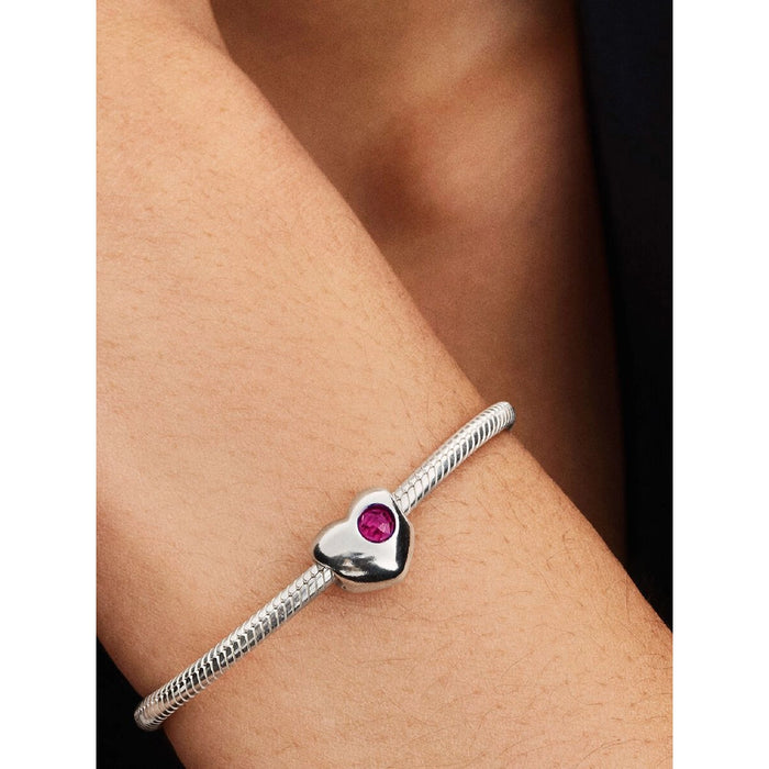 Close-up of a Pandora silver bracelet featuring a heart-shaped charm with a vivid red stone, worn on the wrist.