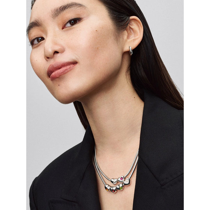 Model wearing layered Pandora necklaces with multiple heart-shaped charms, including one with a white stone.