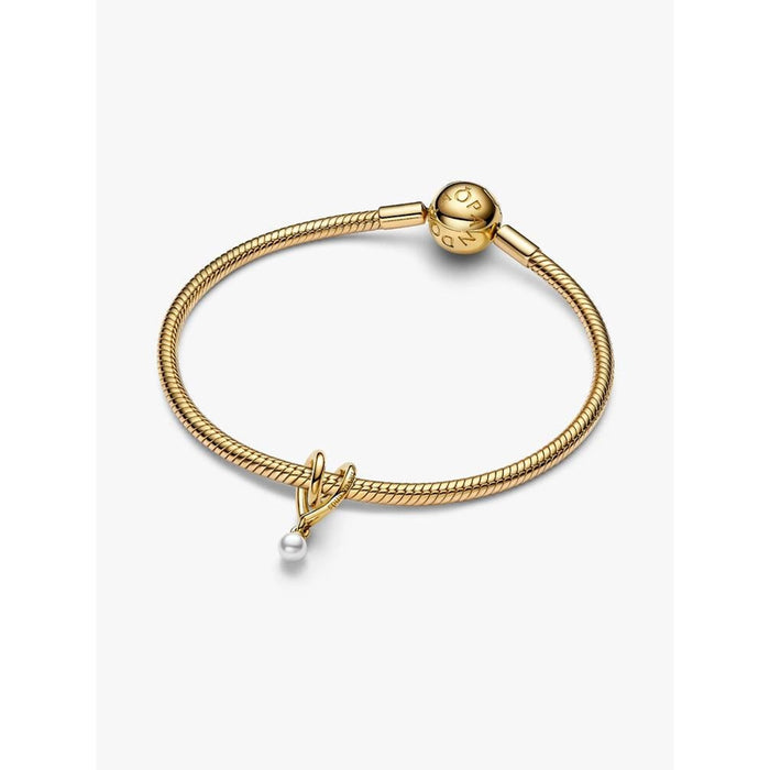 Gold Pandora snake chain bracelet styled with the Wrapped Heart Charm and pearl drop on a white background.