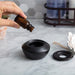 Hand pouring essential oil into a black ceramic diffuser on a marble surface.