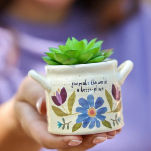 A woman holds a small ceramic pot containing a vibrant succulent plant, showcasing her interest in indoor gardening.