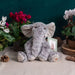 A stuffed elephant rests against a white backdrop, highlighting its cuddly appearance and friendly expression.
