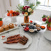 Nora Fleming White ceramic rectangle platter with wavy edge displayed with  Breakfast spread with bacon, pancakes, and fruit on a marble table.