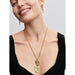 Smiling woman wearing a gold chain necklace with the Pandora Crossing Arrows Medallion Charm layered with other medallion charms, paired with gold link earrings.