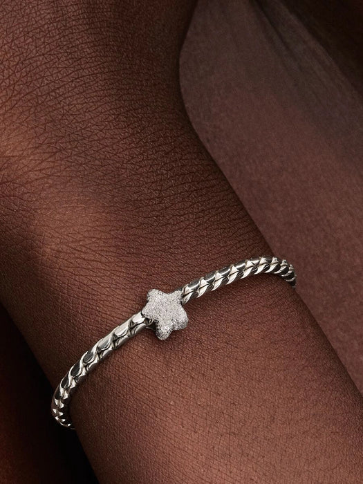 Sterling silver bracelet with a textured star-shaped charm shown on a model’s wrist.