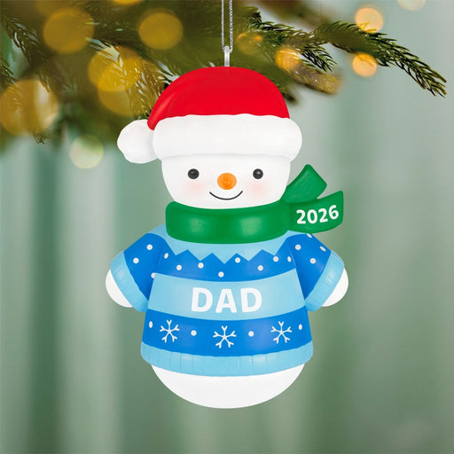 2026 Hallmark Dad snowman ornament hanging on pine branch with golden bokeh lights