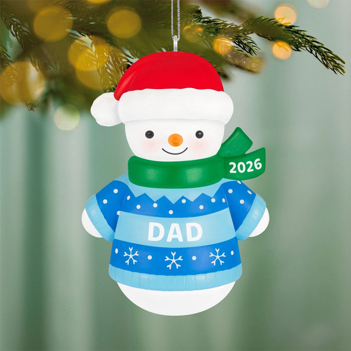 2026 Hallmark Dad snowman ornament hanging on pine branch with golden bokeh lights