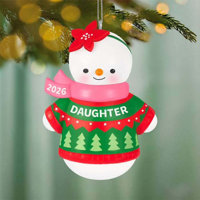 Christmas ornament of a snowman wearing a green sweater with 'DAUGHTER' and a red scarf, hanging on a tree.