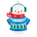 Christmas ornament of a snowman wearing a blue sweater with green trees, red scarf, and green earmuffs on a white background.