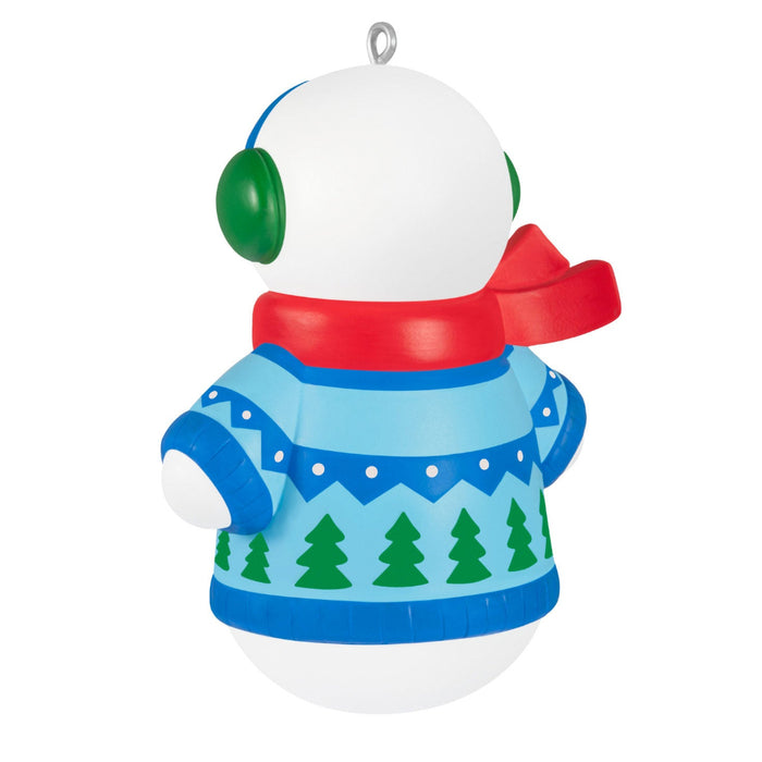 Christmas ornament shaped like a snowman with a blue sweater and green trees, red scarf, and white background.