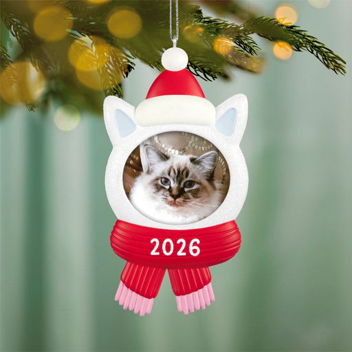 Christmas ornament with a cat's face, Santa hat, and red scarf, hanging on a tree.