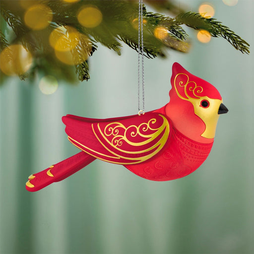Red cardinal ornament hanging on pine branch with gold filigree and warm bokeh background