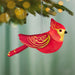 Red cardinal ornament hanging on pine branch with gold filigree and warm bokeh background