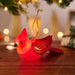 Illuminated red cardinal Christmas tree ornament with gold scrollwork on wooden surface