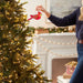 Hand placing illuminated red cardinal ornament on lit Christmas tree near fireplace mantel