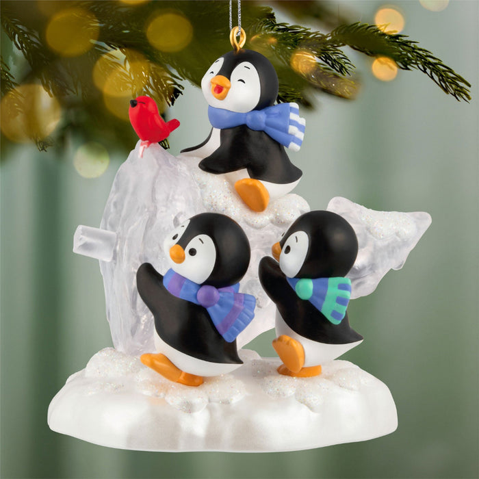 Christmas ornament with penguins and a cardinal on a snowy base, hanging from a tree.