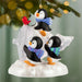Christmas ornament with penguins and a cardinal on a snowy base, hanging from a tree.