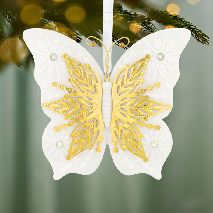 Decorative butterfly ornament with gold and white design on a blurred Christmas tree background