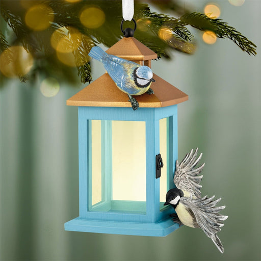 Feathered Friends ornament hanging on evergreen branch with golden bokeh lights