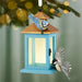 Feathered Friends ornament hanging on evergreen branch with golden bokeh lights
