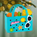 Colorful beach-themed ornament with sand toys and 'Relax' text, hanging against a blurred green background.