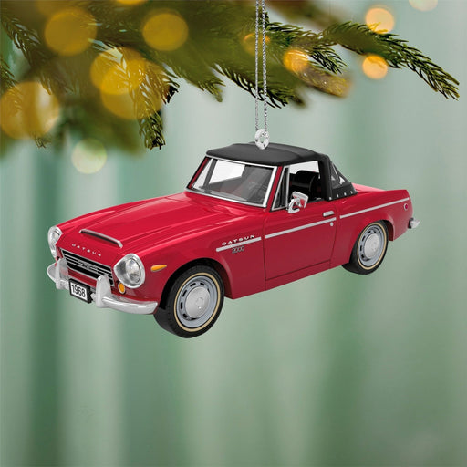 Cherry red 1968 Datsun 2000 Sports Christmas ornament with black soft top and turning wheels hanging on pine tree