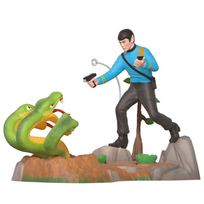 Figurine of a character in a blue shirt and black pants standing on a rock with a green snake and a gun.
