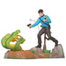 Figurine of a character in a blue shirt and black pants standing on a rock with a green snake and a gun.