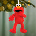 Red textured fur-like Tickle Me Elmo ornament hanging on green pine branch with golden lights