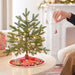 Small decorated Christmas tree on a table with a person adding an ornament.