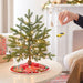 Small decorated Christmas tree with a hand placing a yellow car ornament on a table.