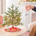 Small decorated Christmas tree on a table with a person hanging a ornament.