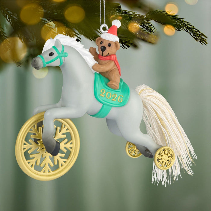 Gray plastic pony ornament with teddy bear rider hanging on pine branch with bokeh lights