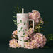A floral mug in pink and green hues, complete with a straw, showcasing a cheerful design.