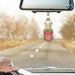A car air freshener bottle with a red label hangs from a beige coiled string beneath a rearview mirror in a car, with a blurred road and trees in the background.