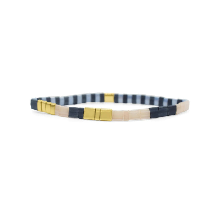 A bracelet featuring striped fabric and gold-tone metal accents, showcasing a stylish and modern design.