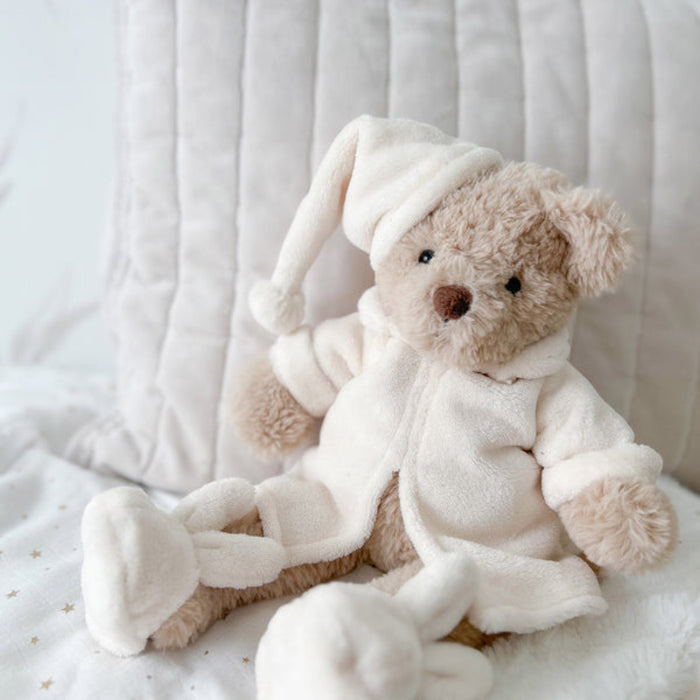 Teddy bear in pajamas sitting on a white blanket