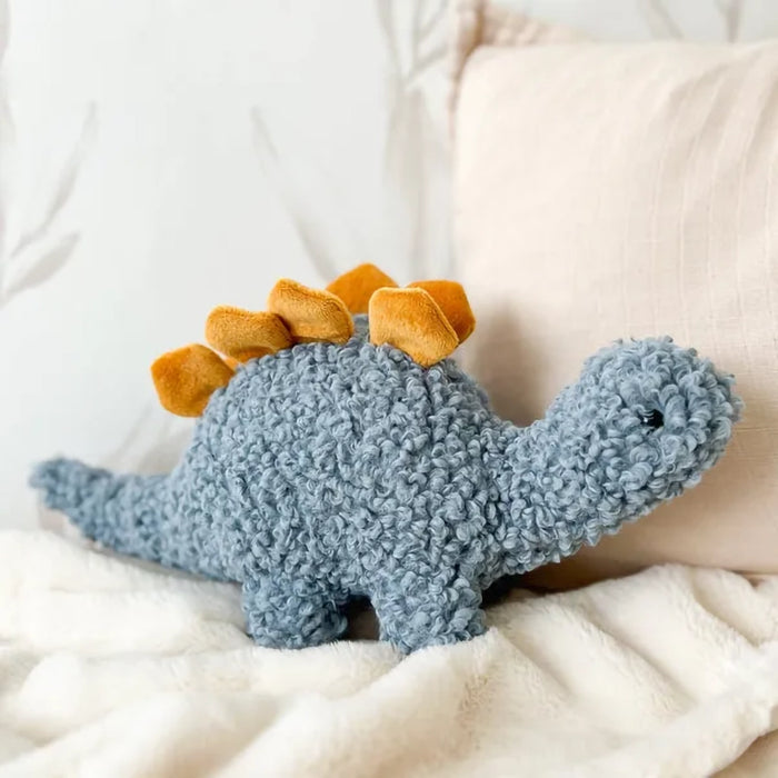 Gray plush stegosaurus toy with golden plates resting on a cream blanket beside a beige cushion