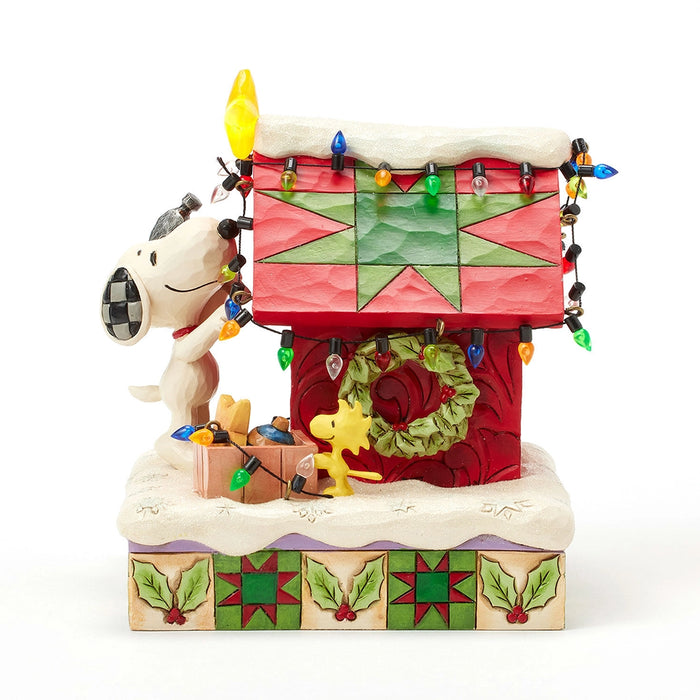 Side view of Snoopy and Woodstock decorating the doghouse with multicolored lights and a green wreath.