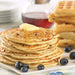 Stack of fluffy blueberry pancakes topped with melting butter, fresh blueberries, and golden waffles in the background, served with maple syrup.