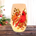 Pre-lit frosted glass vase with two cardinals perched on holly branches glowing warmly on a wood surface.
