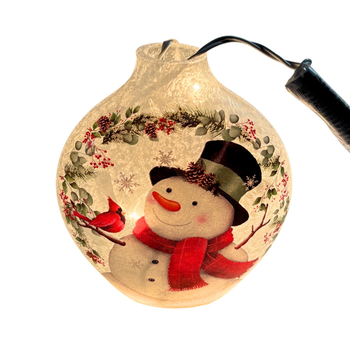 Close-up of a Stony Creek circular pre-lit vase featuring a smiling snowman with a red scarf and top hat surrounded by holiday greenery and a cardinal.