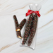 Sweet jubilee dark chocolate covered caramel Pretzel Rods with sprinkles in a clear bag with a red ribbon on a marble surface