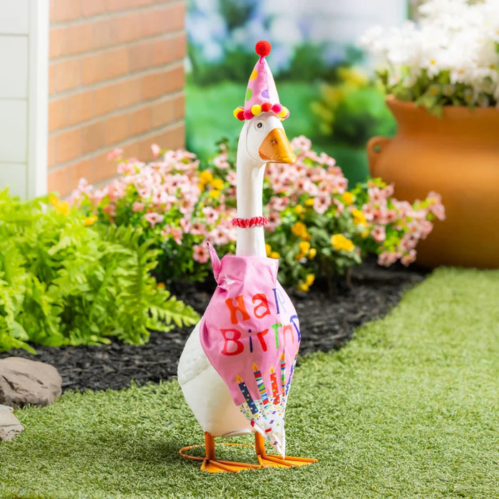 A duck wearing a colorful birthday hat stands on a green lawn, celebrating a festive occasion.