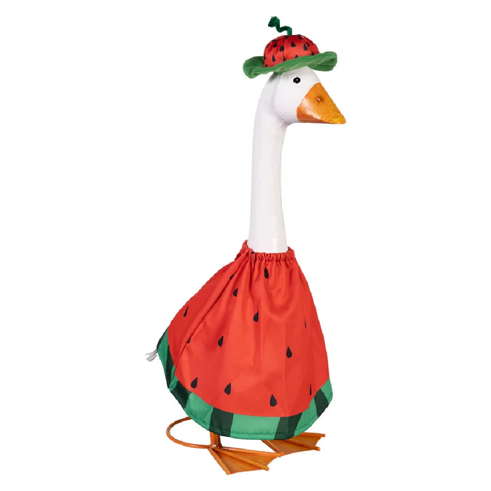 A duck dressed in a watermelon-themed outfit stands amidst a flourishing garden, adding charm to the scene.