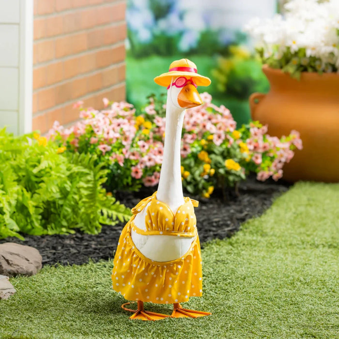 A stylish duck wearing a dress and hat poses in a lush garden surrounded by blooming plants.